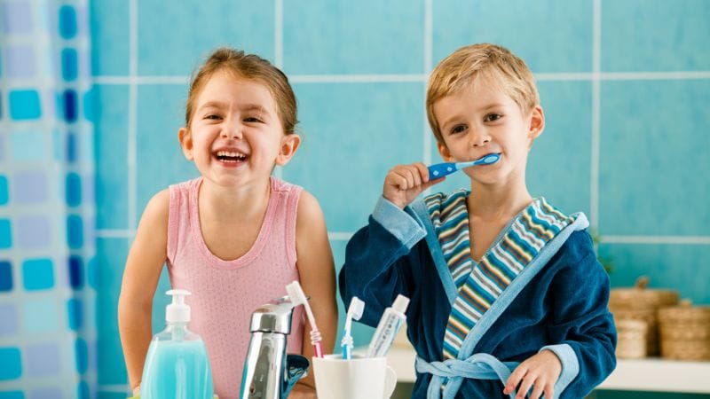 Two young children looking in the mirror whilst brushing their teeth