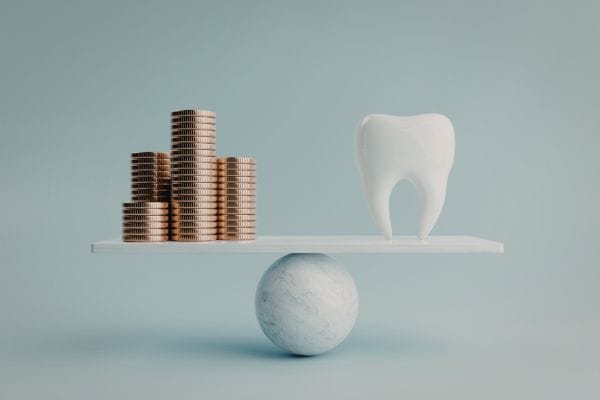 scales with coins piled up on one side and a tooth on the other signing the question how much do dental implants cost in the UK